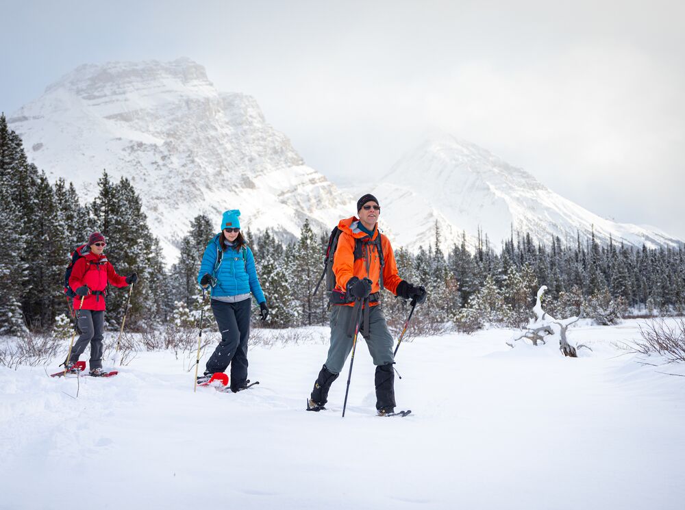 Three peopel going on a snowshoeing adventure in Banff National Park with mountains in the background.